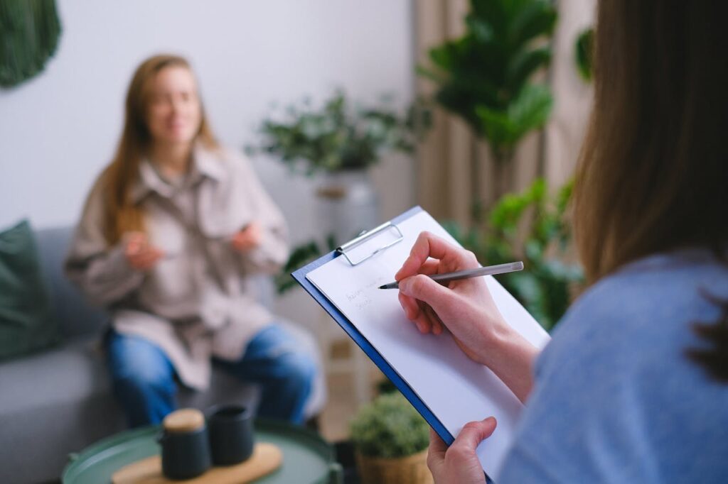 pexels-photo-7176026 Unrecognizable professional female psychologist writing on clipboard while sitting against client on blurred background during psychotherapy session in light office