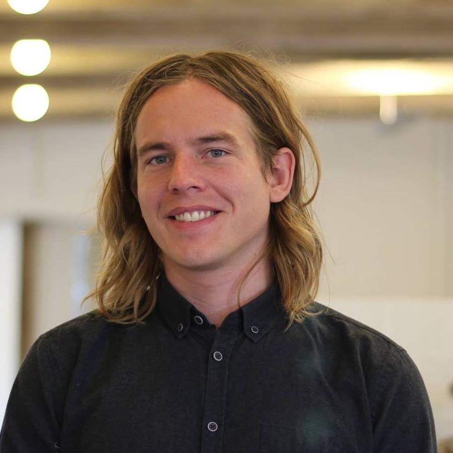 Mand med langt hår og skjorte Mand med langt, bølget hår iført en sort skjorte, der smiler til kameraet.